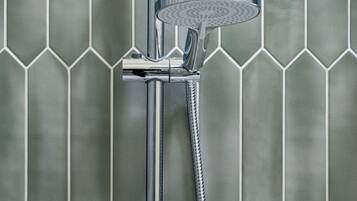 Douche met een handdouche en flexibele slang, bevestigd aan een wand met een mozaïek van zeshoekige tegels.