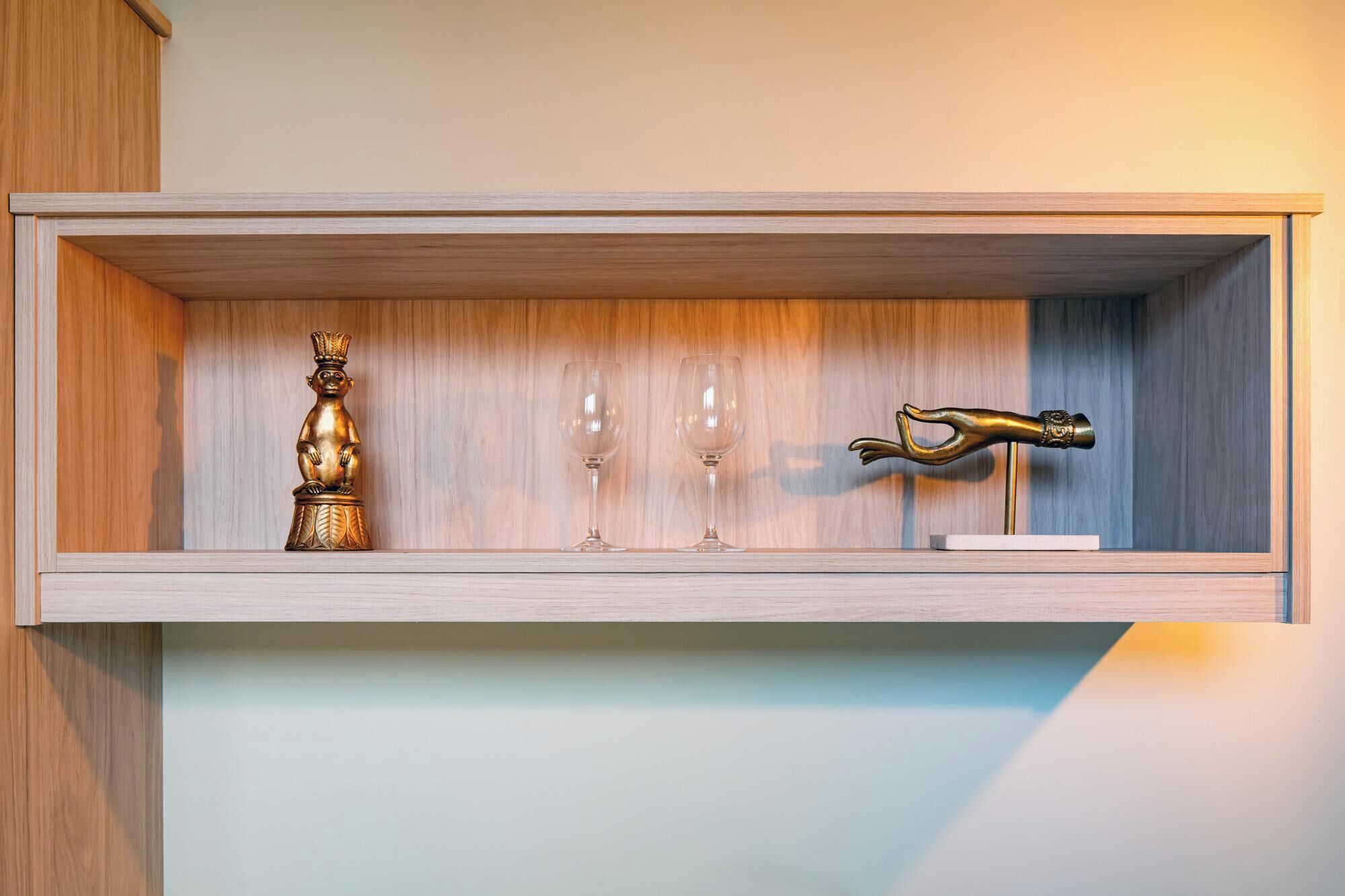 A shelf with a golden statue, two wine glasses, and a brass door handle.