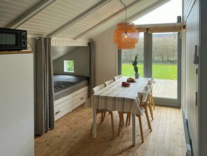 A compact room with a bed, dining table, chairs, a hanging light fixture, and a view through a glass door. - Summer house 344 steps from beach near Saksild (Odder)