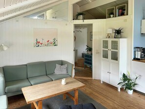 Una sala de estar con un sofá, una mesa de centro de madera, un cuadro, un aparador con puertas de vidrio y una escalera que conduce a un nivel superior.