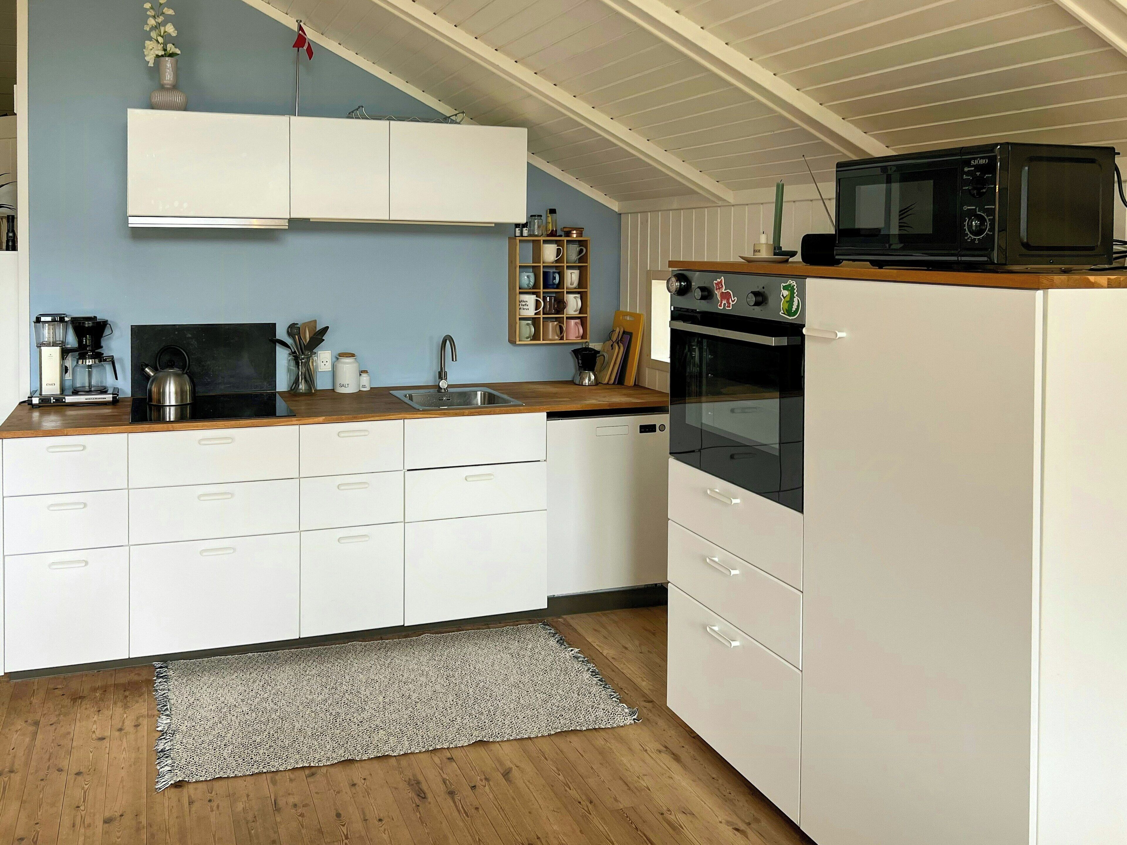A kitchen with white cabinets, a wooden countertop, a microwave, a kettle, and a coffee maker.