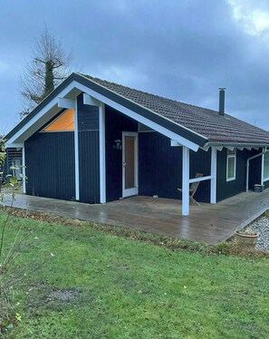 Una casa moderna con fachada oscura, techo inclinado y una terraza de madera.