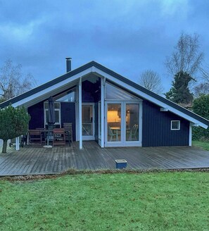 A modern house with a sloped roof, large glass doors leading to an interior, and a wooden deck. - Summer house 344 steps from beach near Saksild (Odder)