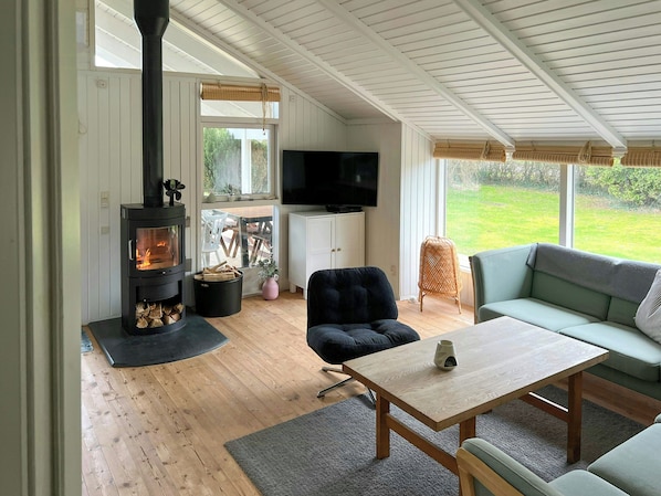 A cozy living room with a wood-burning stove, a television, a sofa, and a dining table. - Summer house 344 steps from beach near Saksild (Odder)