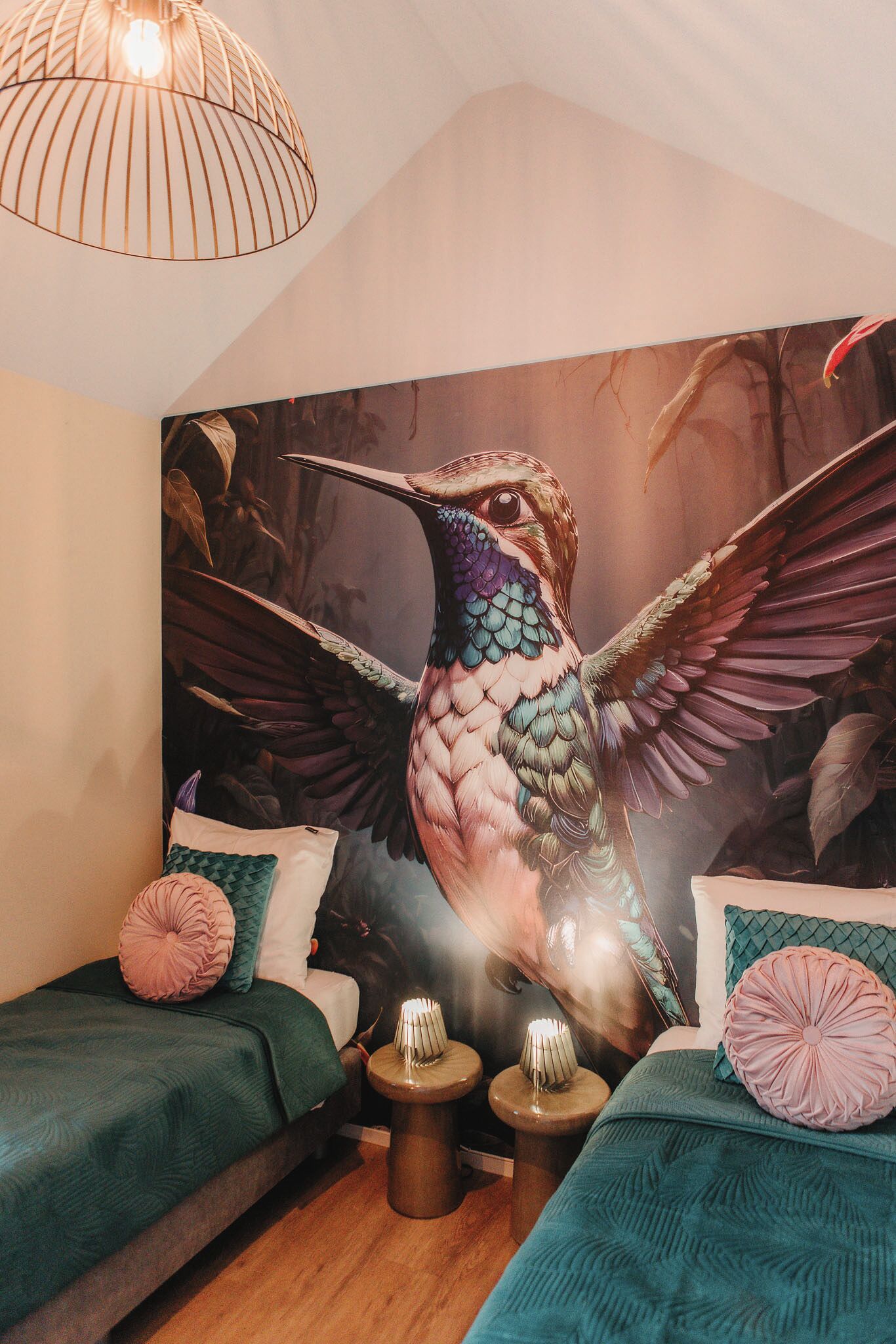 A bedroom with two beds, a large mural of a hummingbird, and a unique pendant light.