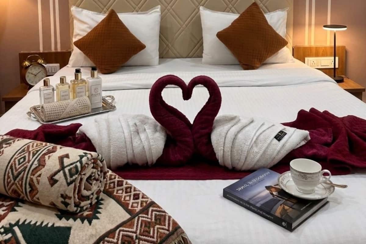 Hotellihuone, jossa on sänky, tyynyjä, pieni tarjotinalusta, jossa on hygieniatuotteita, sydämenmuotoinen pyyheasetelma, peitto, kuppi ja kirja.
