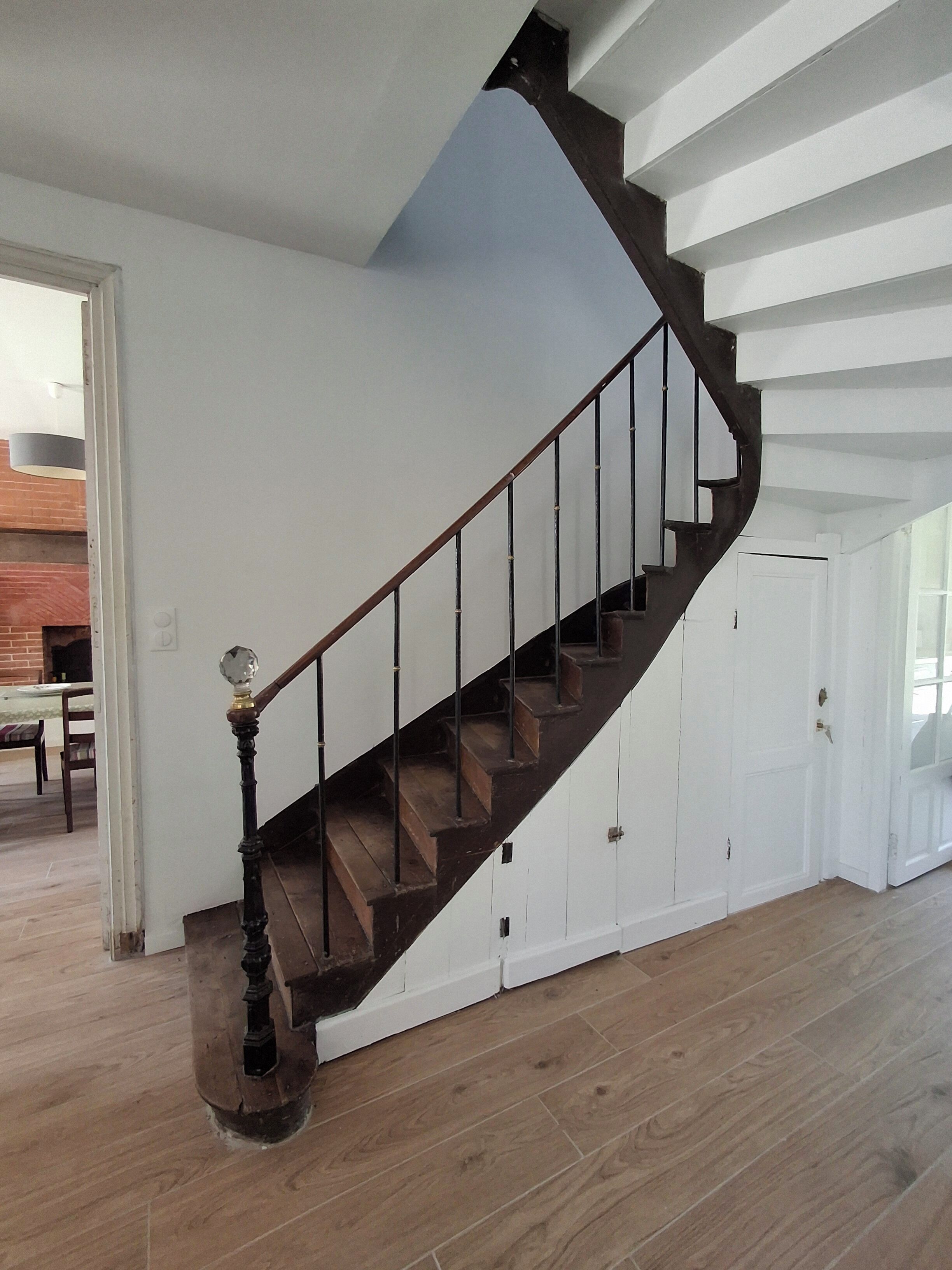 Eine Holztreppe mit dunkler Oberfläche, weißen Wänden und einer Tür am Fuß.
