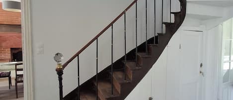 Eine Holztreppe mit dunkler Oberfläche, weißen Wänden und einer Tür am Fuß.