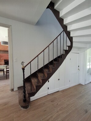 A wooden staircase with a dark finish, white walls, and a door at the bottom. - Ty Coq • Authentic Breton home - 1650 (Plouescat)