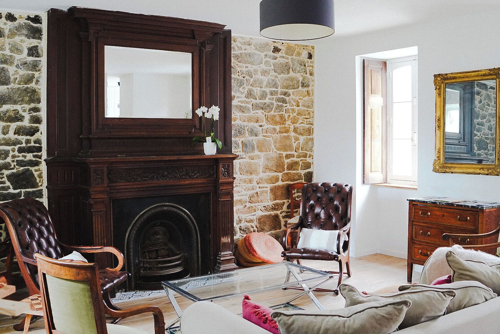 A room with a stone wall, a fireplace, a mirror, a sofa, and a chair.