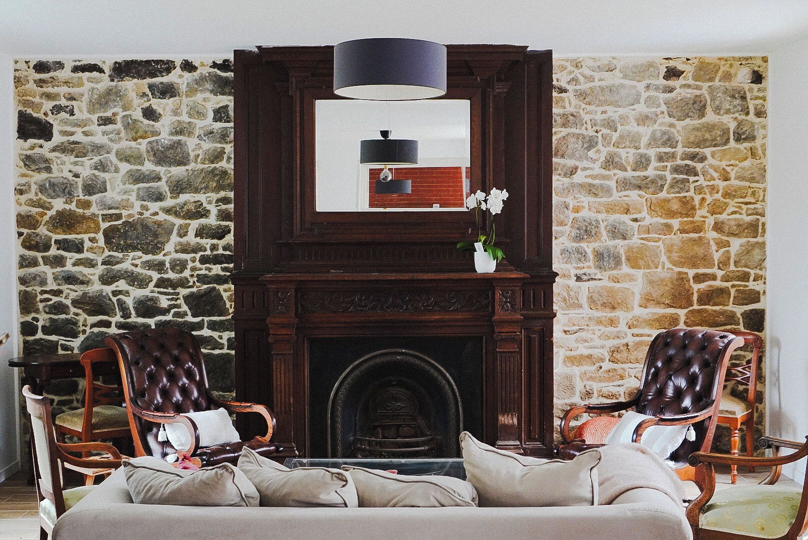 A room with a stone wall, a fireplace, two leather armchairs, a sofa, and a hanging light fixture.
