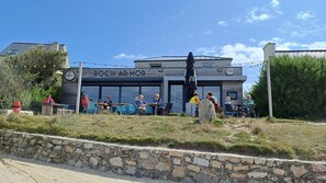 A restaurant with outdoor seating, a stone wall in the foreground, and a clear sky. - Ty Coq • Authentic Breton home - 1650 (Plouescat)