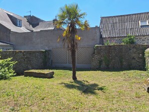 A grassy yard with a palm tree, stone walls, and a building with a tiled roof. - Ty Coq • Authentic Breton home - 1650 (Plouescat)