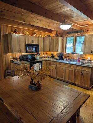A wooden cabin-style kitchen with a central island, wooden cabinets, and a window overlooking the forest. - Picture Rocks Log Cabin (Picture Rocks)