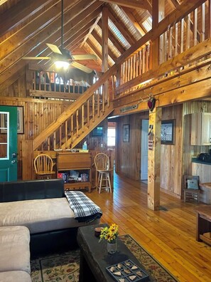 A spacious loft with a wooden staircase, a cozy seating area, and a kitchen in the background. - Picture Rocks Log Cabin (Picture Rocks)