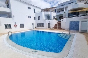 A swimming pool with a clear blue water, surrounded by white buildings with balconies and a staircase leading to an upper level. - Tranquil Hillside Apartment – Sea View, Pool & Mountains – Los Cristianos (Arona)