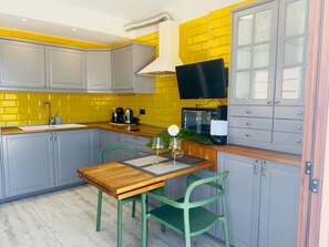 A kitchen with a wooden table, two chairs, a TV, and cabinets. - Tranquil Hillside Apartment – Sea View, Pool & Mountains – Los Cristianos (Arona)