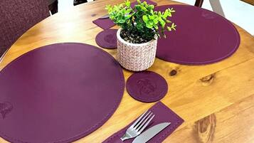 A round wooden table with purple placemats, a small potted plant, and cutlery on a napkin.
