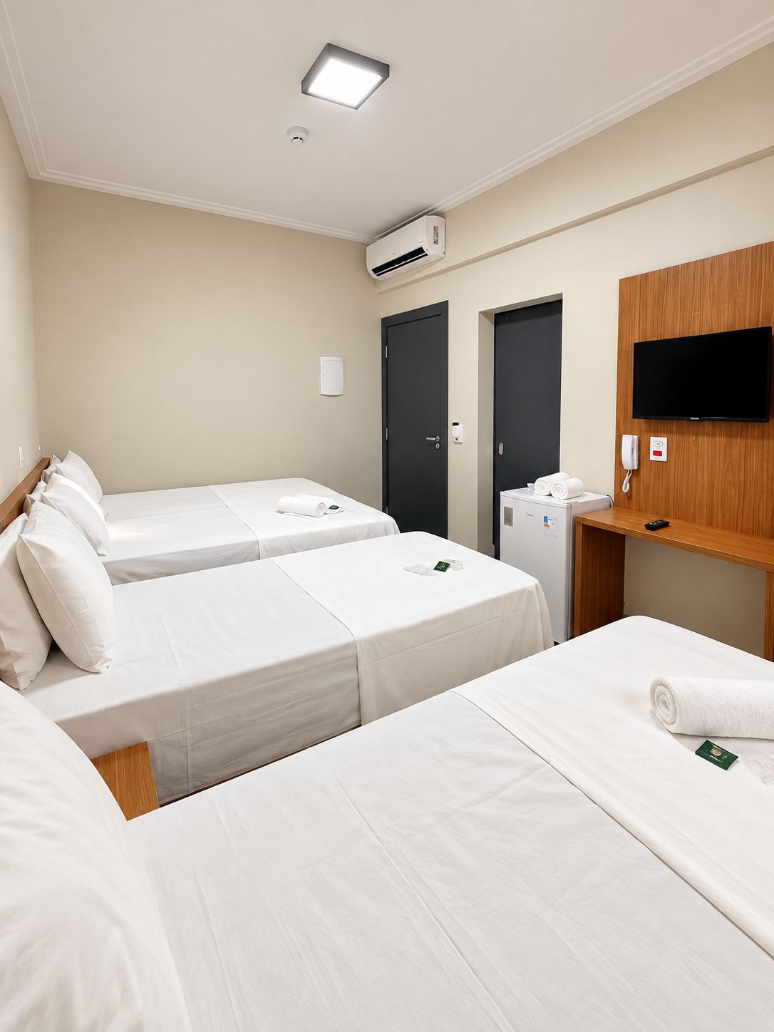 Habitación de hotel con dos camas individuales, un televisor montado en un panel de madera, un escritorio con teléfono y un equipo de aire acondicionado en la pared.