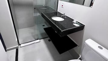 A modern bathroom with a glass shower enclosure, a black countertop sink, and a white toilet.