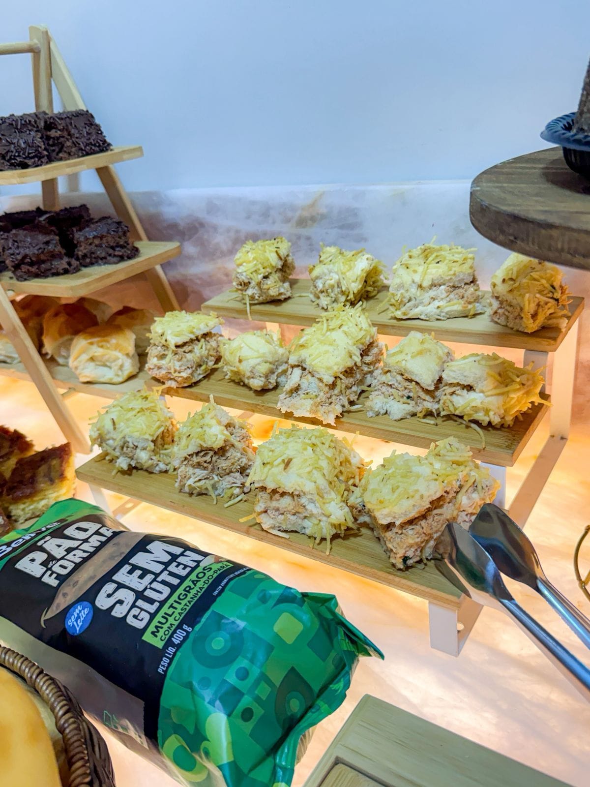 A display of food items on a wooden stand with a bottle of 'Pão de Queijo' in the foreground.