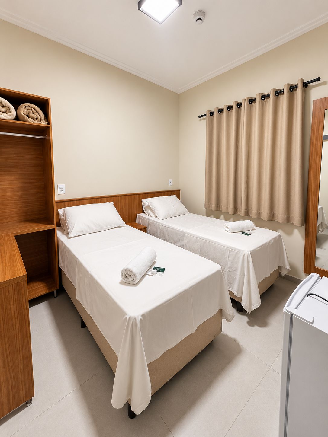 A hotel room with two beds, a wooden wardrobe, a small table, and a mirror.