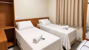 A hotel room with two beds, a wooden wardrobe, a small table, and a mirror.