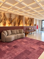 Um lobby moderno com sofá seccional, plantas decorativas e carpete estampado.