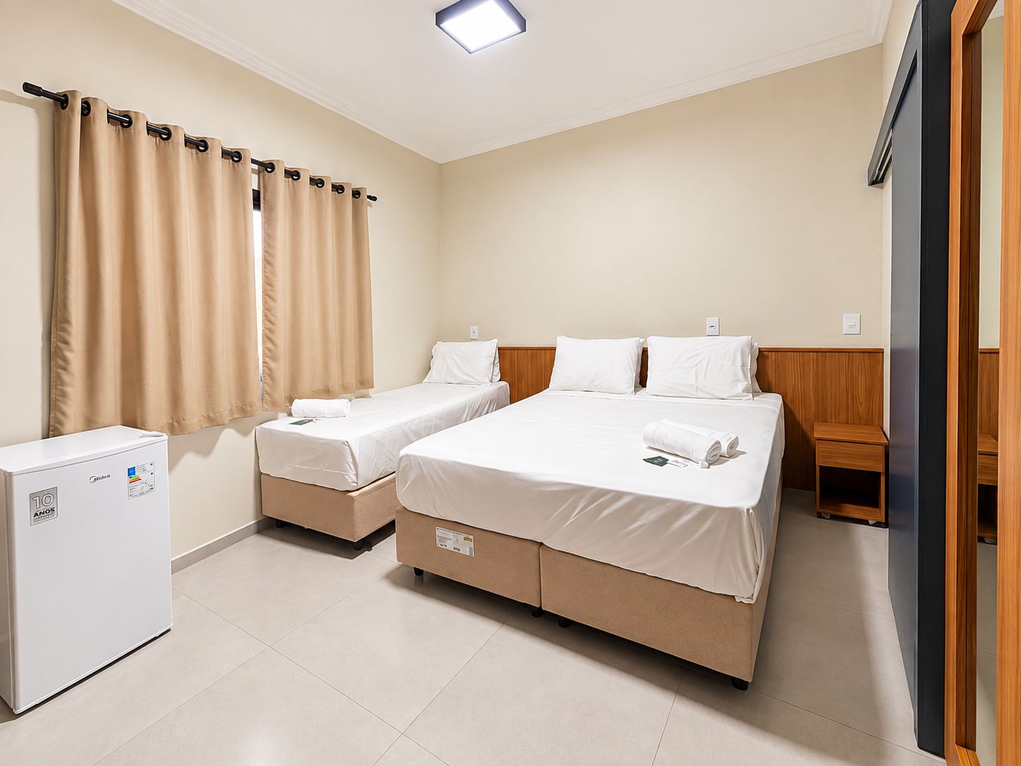 Habitación de hotel con dos camas, un refrigerador pequeño y un armario de madera.