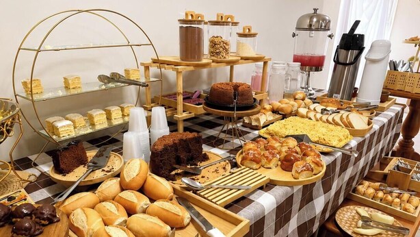 A buffet table with various food items, utensils, and containers. - Missal Hotel (Aparecida)