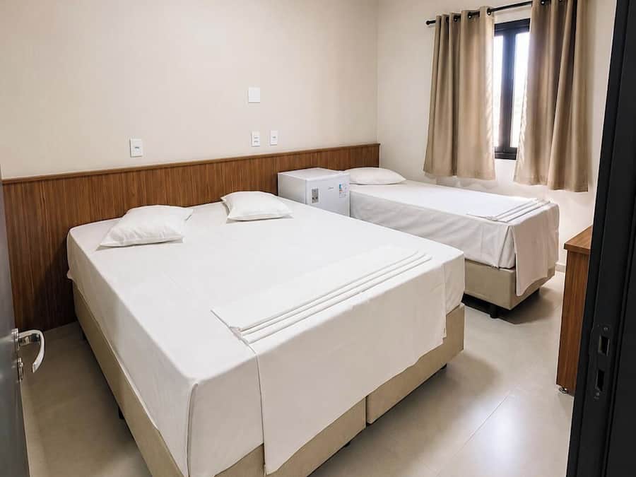 Habitación de hotel con dos camas, cabecero de madera, un escritorio pequeño y una ventana con cortinas.