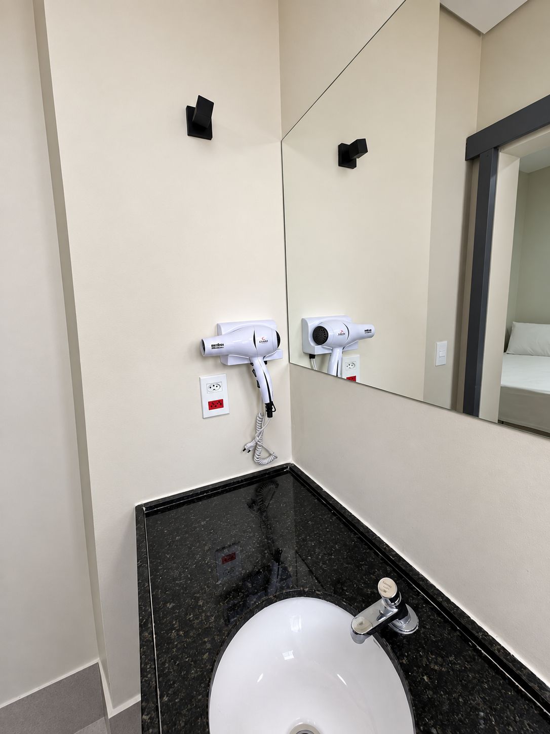 A bathroom with a black marble sink, a white basin, and two hair dryers mounted on the wall.