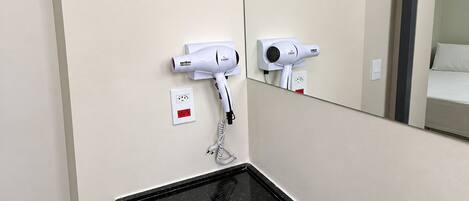 Une salle de bain avec un lavabo en marbre noir, un bac blanc et deux sèche-cheveux fixés au mur.