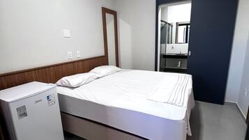 Habitación de hotel con cama, un refrigerador pequeño, un espejo y una puerta que da a un baño.