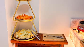 Uma mesa de madeira com um suporte dourado para frutas em níveis, uma tábua de corte e uma cesta de bananas.