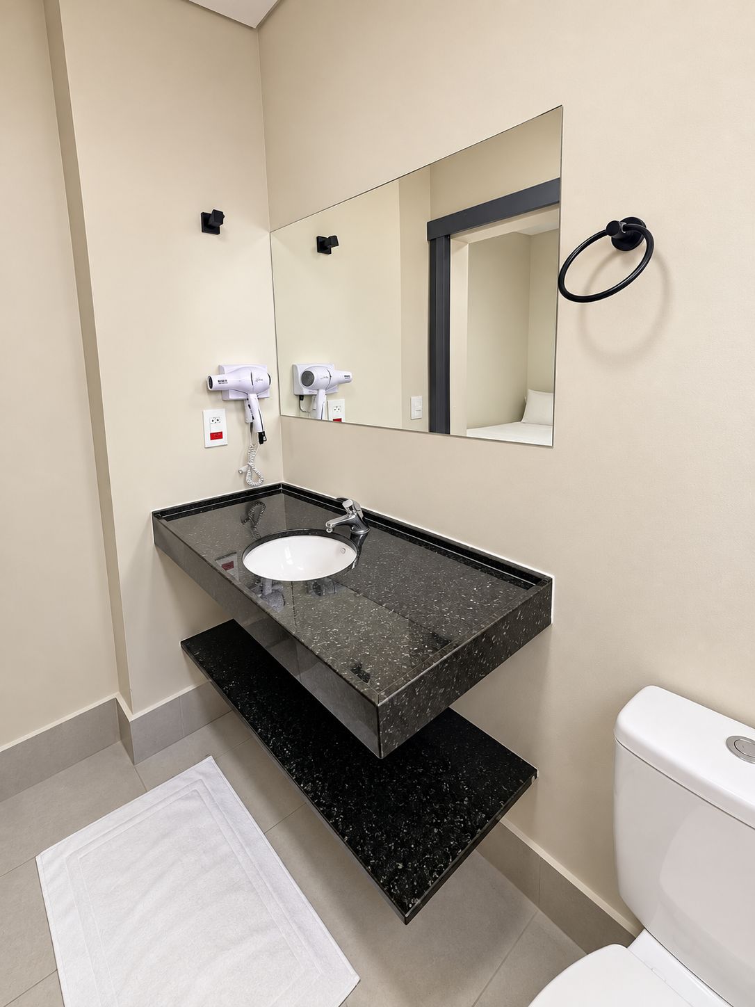 A modern bathroom with a black granite sink, a white toilet, and a mirror above the sink.
