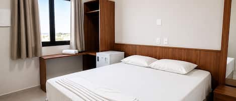 A hotel room with a bed, a desk, a wardrobe, and a window with curtains.
