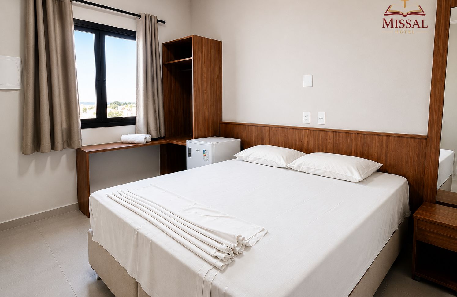 Una habitación de hotel con cama, escritorio, armario y ventana con cortinas.