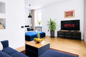 Ein modernes Hotelzimmer mit Bett, Fernseher, Pflanze und Obstschale.