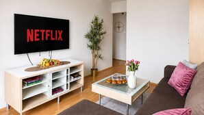 Ein modernes Wohnzimmer mit einem Flachbildfernseher, einer Holzunterhaltungsecke, einem braunen Sofa, einem Couchtisch und einem Blumentopf.