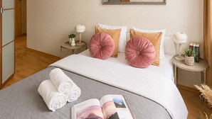 Ein ordentlich eingerichtetes Schlafzimmer mit einem Bett, Kissen, einem Nachttisch mit Lampe, einem Spiegel und einem Buch auf dem Bett.