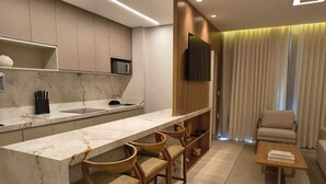 Una cocina moderna con encimera de mármol, taburetes de bar de madera, un televisor de pantalla plana y una zona de estar con sofá y sillón.