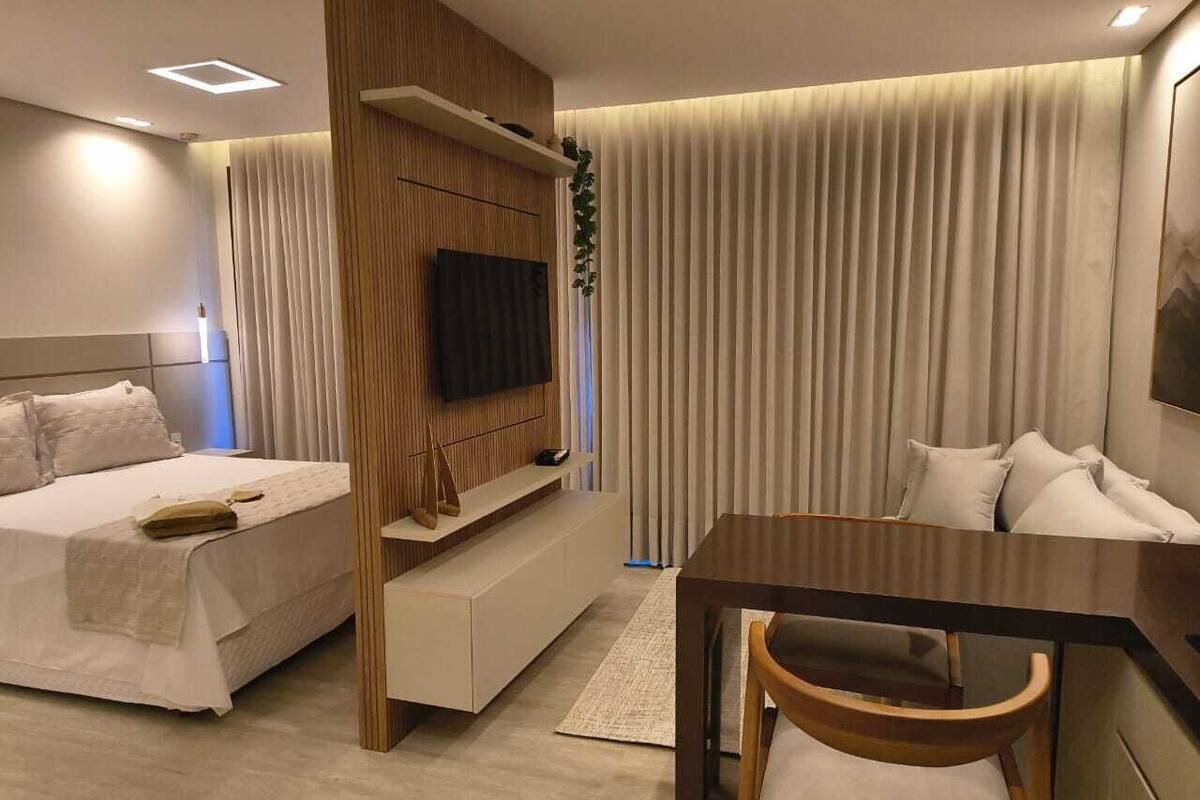 Una habitación de hotel moderna con cama, escritorio, silla, televisor y un ventanal con cortinas.