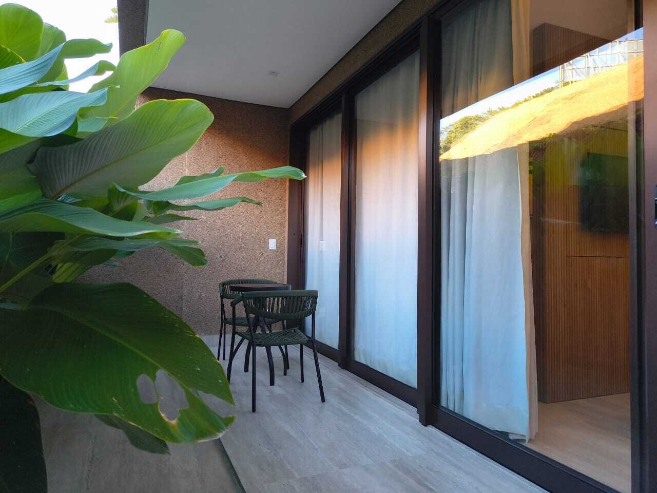 A balcony with a table and chairs, a large plant, and a sliding glass door.
