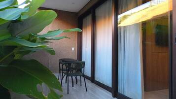A balcony with a table and chairs, a large plant, and a sliding glass door.