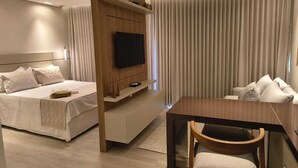 Una habitación de hotel moderna con una cama, un televisor montado en un panel de madera, una mesa de comedor con una silla y un sofá.