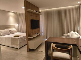Una habitación de hotel moderna con una cama, un televisor montado en un panel de madera, una mesa de comedor con una silla y un sofá.