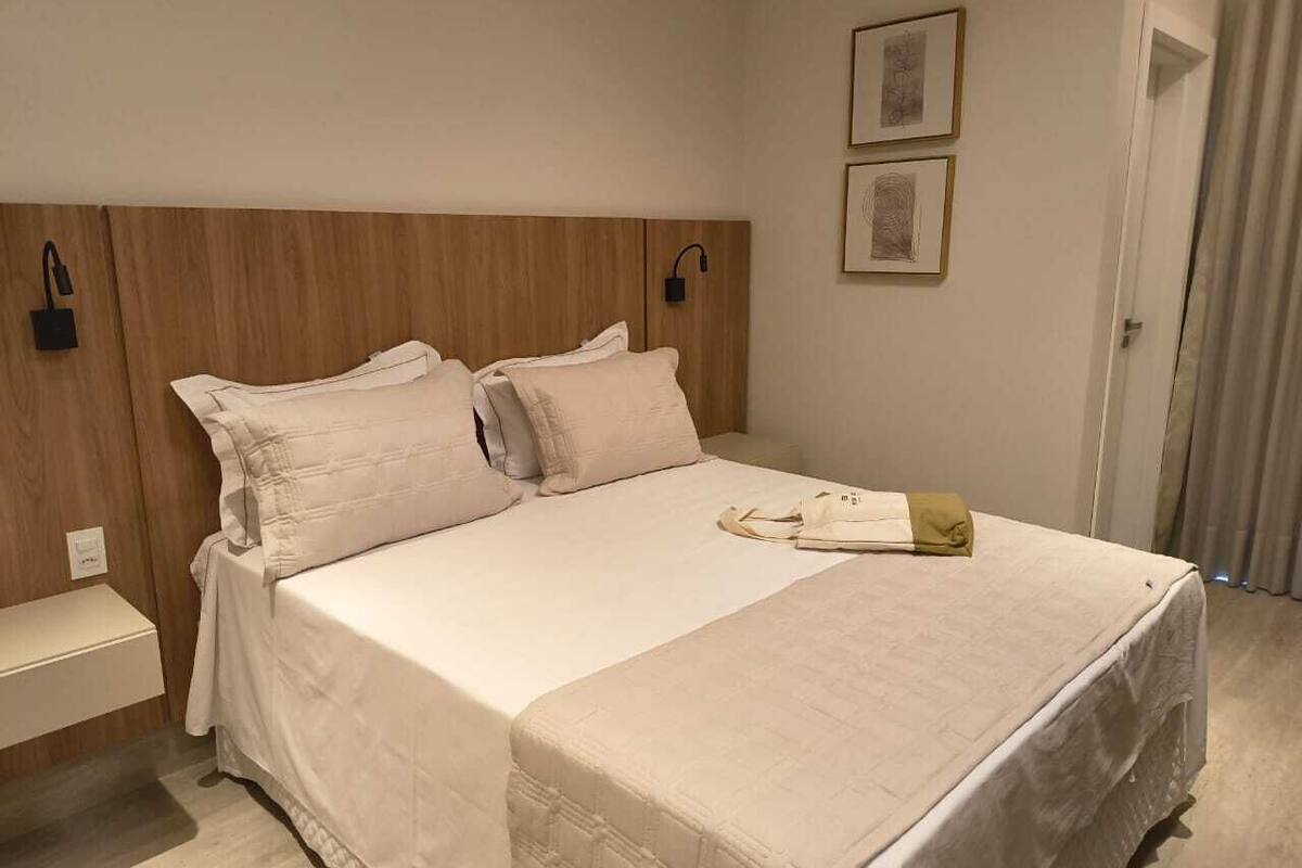 Una cama bien hecha con cabecera, una mesita de noche y dos lámparas de pared.