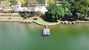 An aerial view of a lake with a dock, surrounded by greenery and buildings.