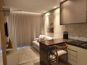 A modern kitchen with a dining area, a sofa, and a large window with blinds.